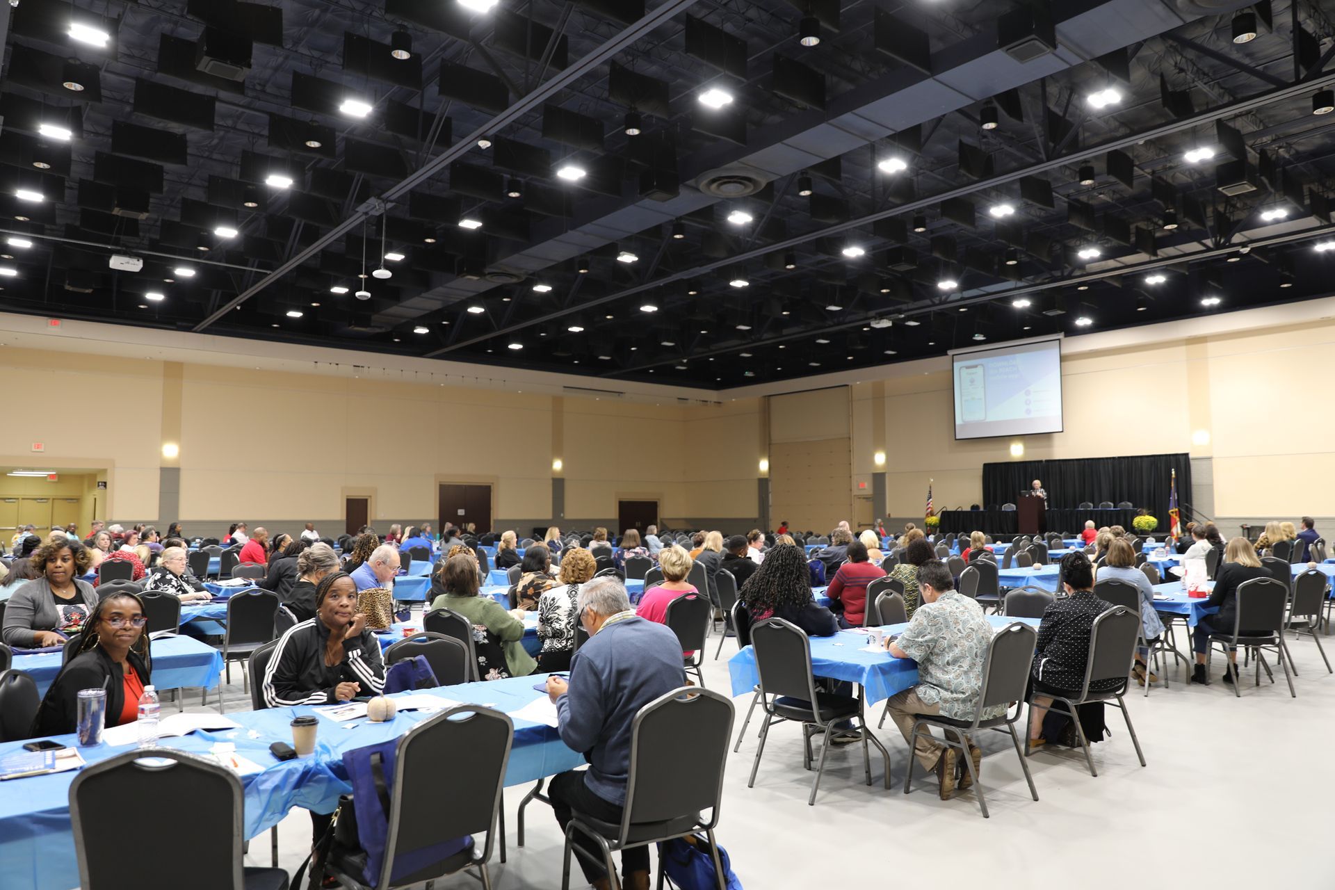 A large room filled with people sitting at tables and chairs.