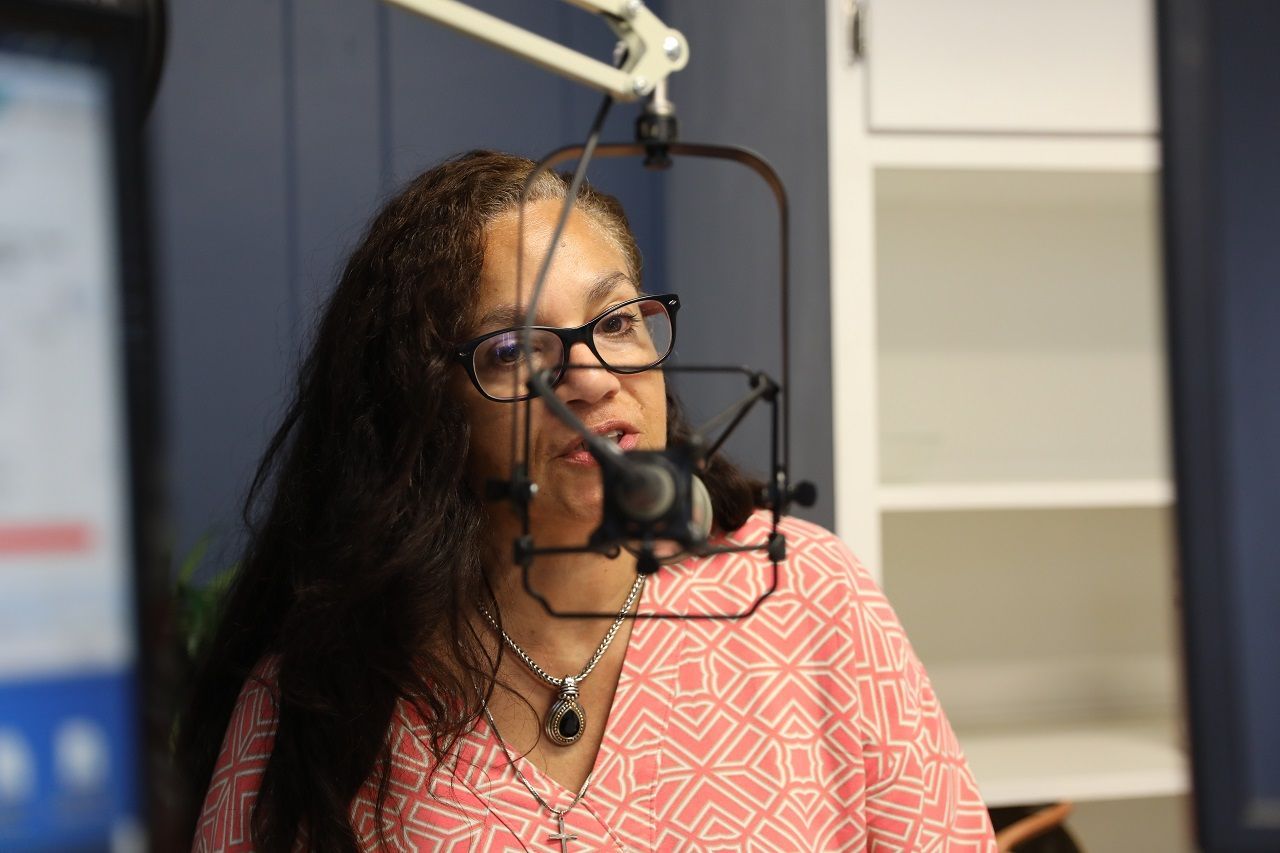A woman wearing glasses is standing in front of a microphone.