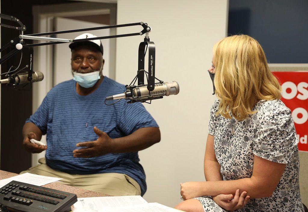 A man wearing a mask is talking to a woman in front of a microphone