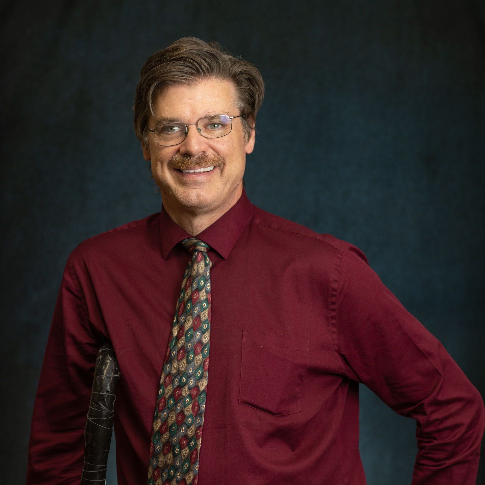 A man in a red shirt and tie is smiling for the camera.