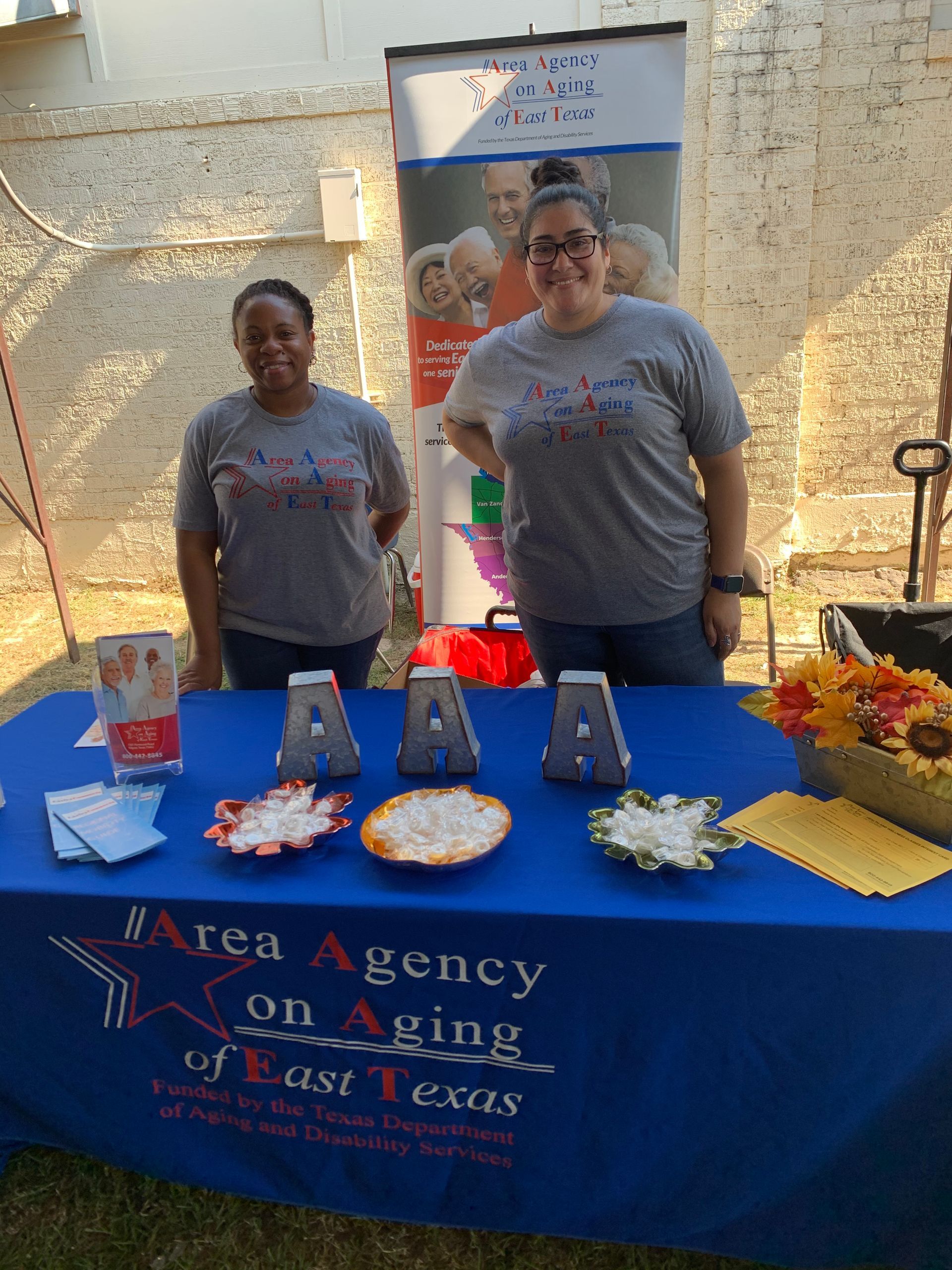 Two women standing behind a table that says ' aren agency on aging of west texas ' on it