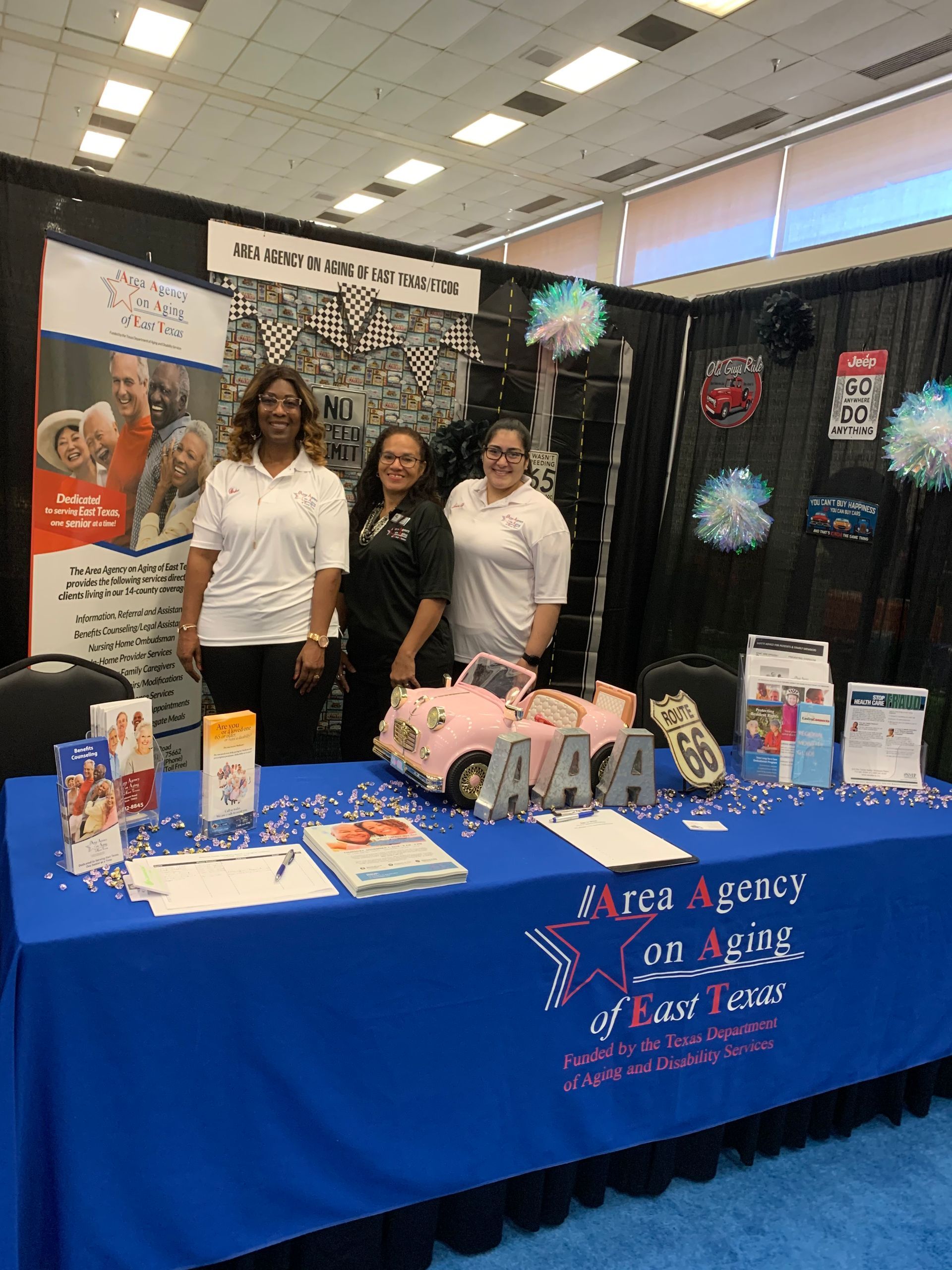 Three women are standing in front of a table at a convention.
