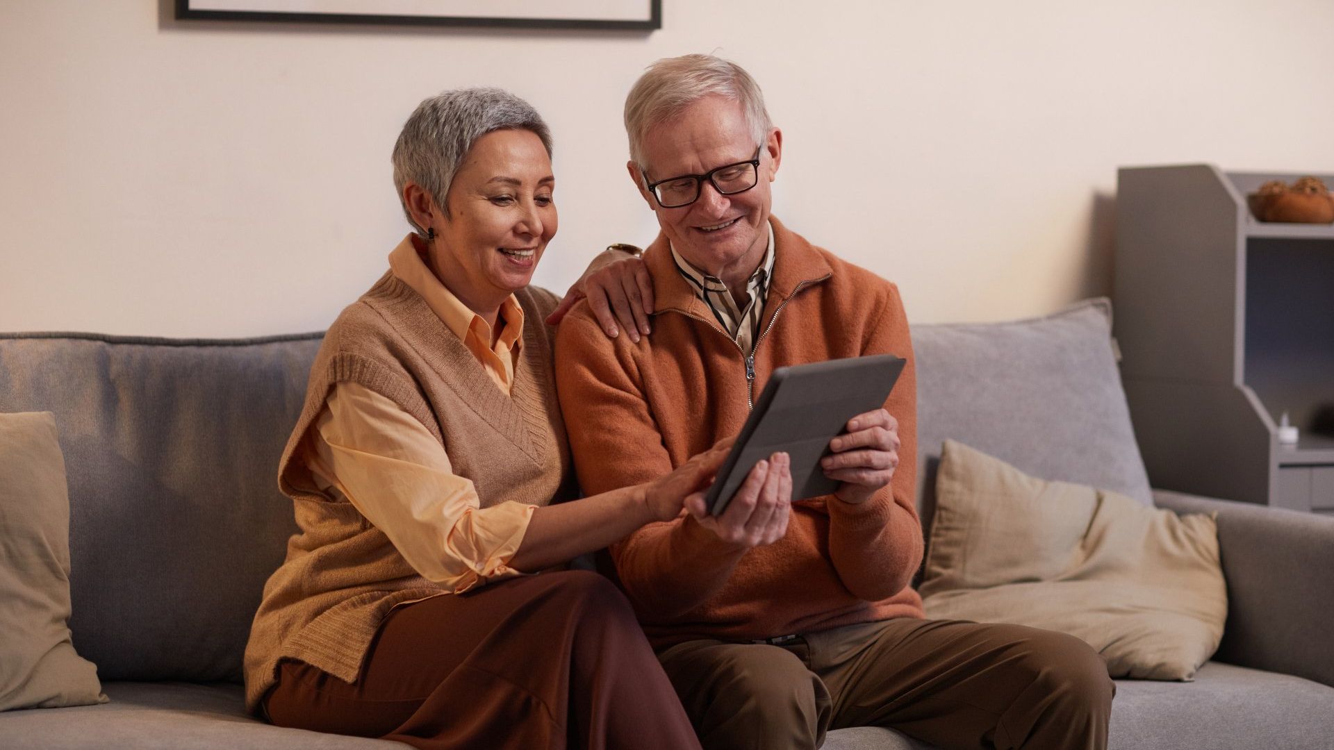Man and women sitting on a couch looking at a tablet.