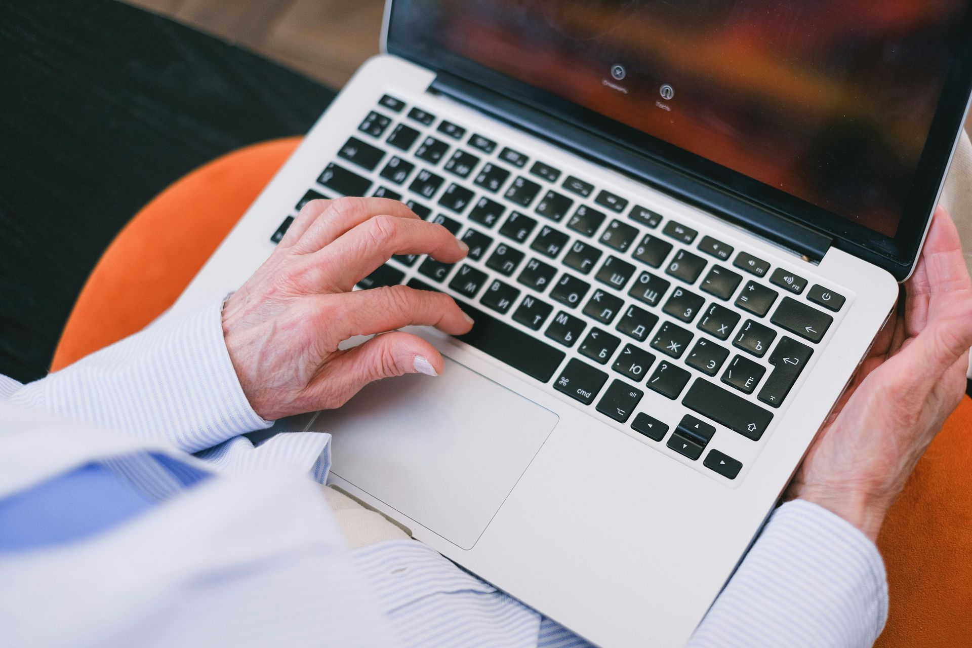 A person wearing a light blue shirt uses a laptop while sitting on an orange circular seat.