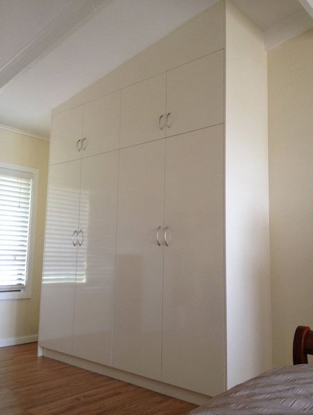 A bedroom with a large white wardrobe and a bed.