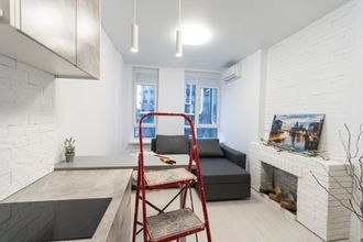 A red step ladder stands in a modern, white kitchen and living area with a grey couch and a brick fireplace.