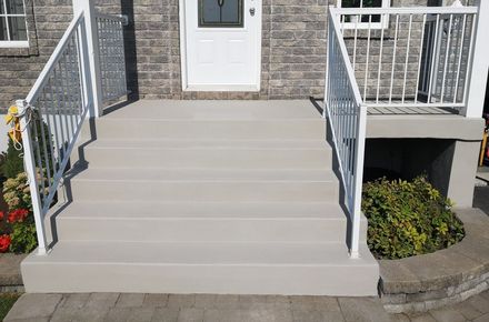 Concrete front porch steps painted light gray with white metal railings leading to a house entrance.