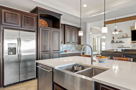 Modern kitchen with stainless steel appliances, dark wood cabinets, white countertops, and a double basin sink.