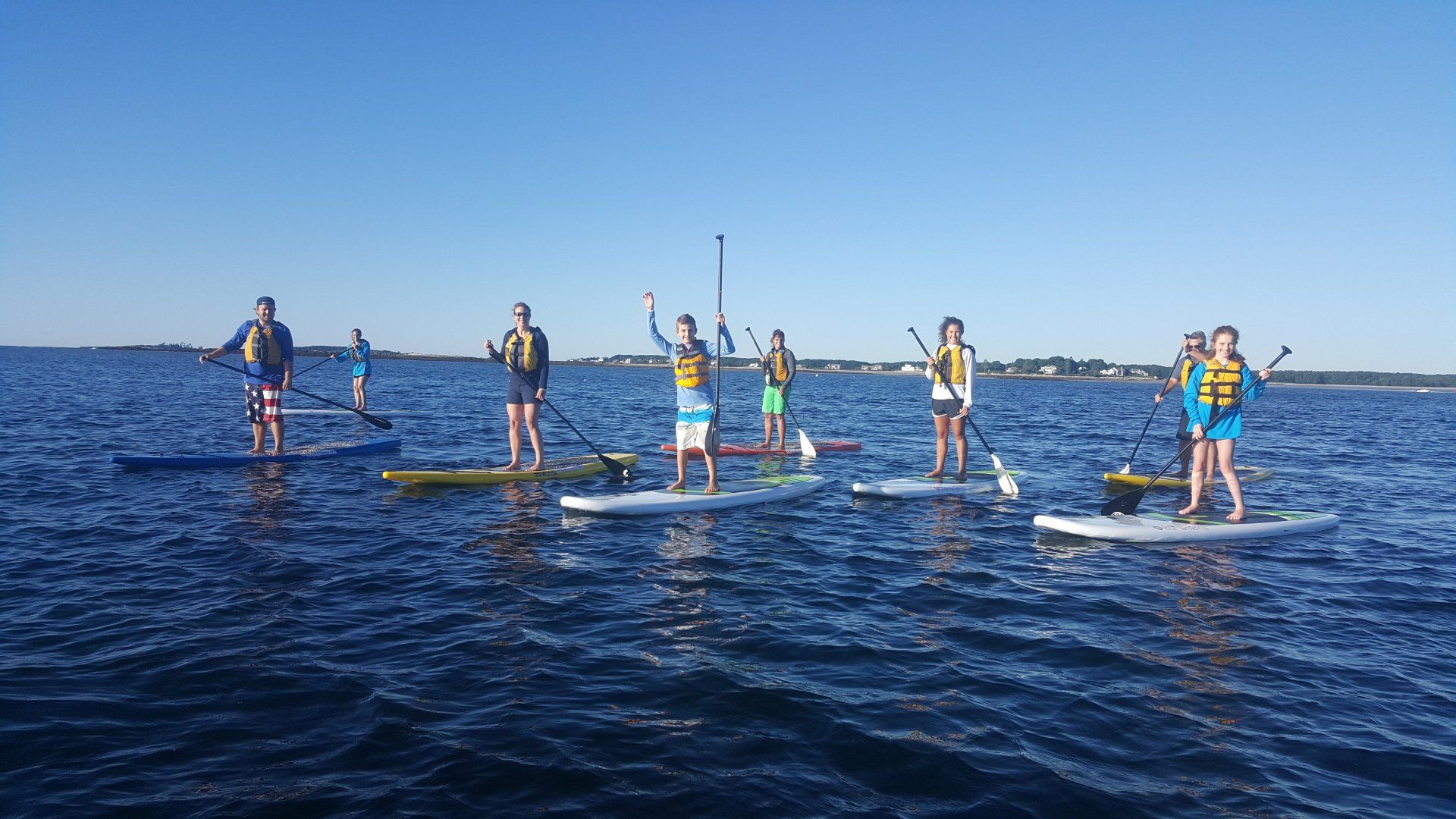 Group of people on stand up paddle board while other raising their hand