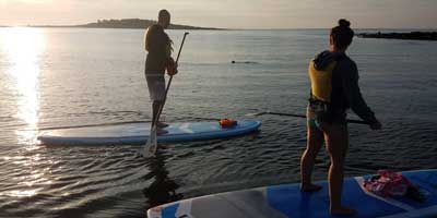 Man and woman on stand up paddle board while on sunset