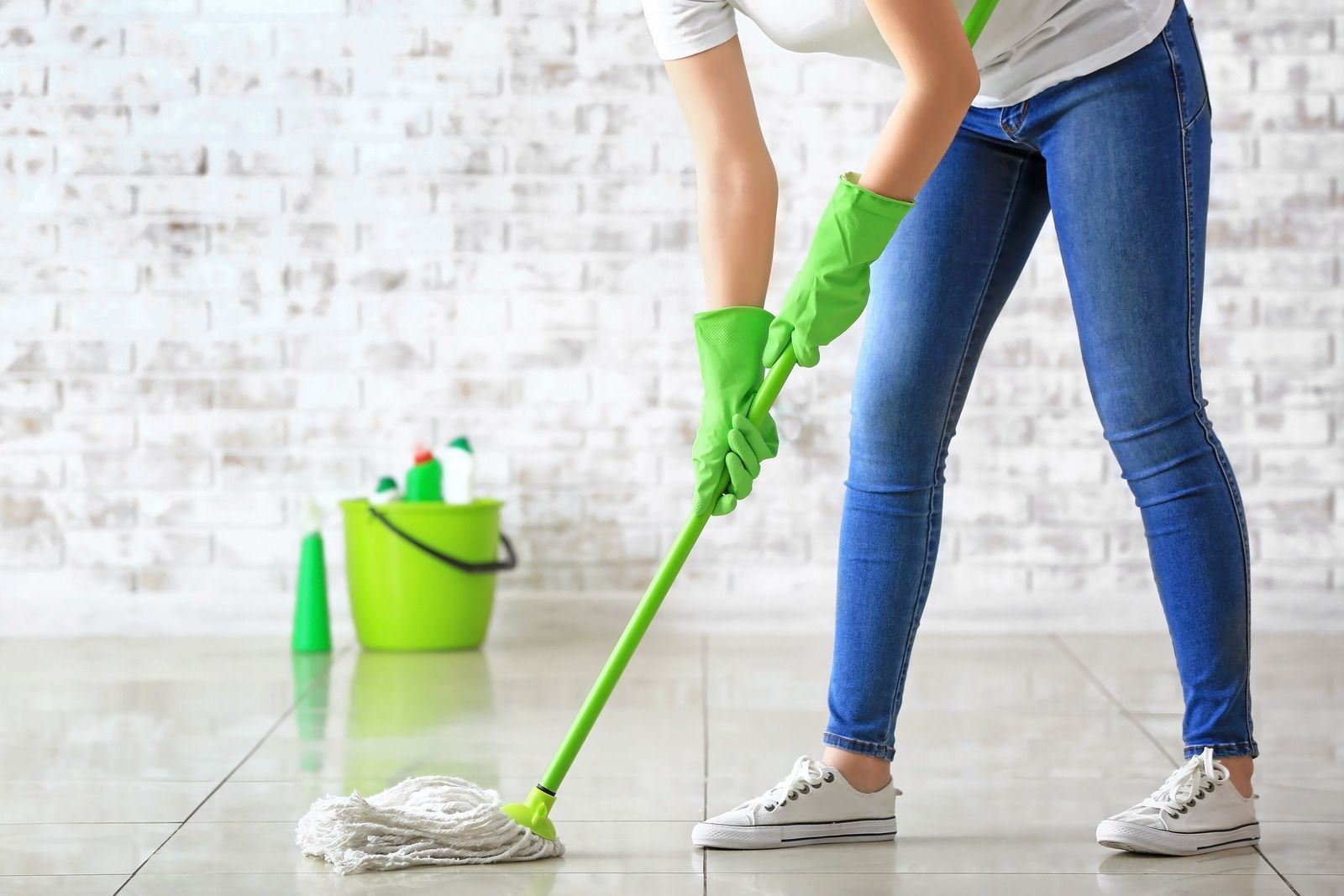 A woman in green gloves is cleaning the floor with a mop.
