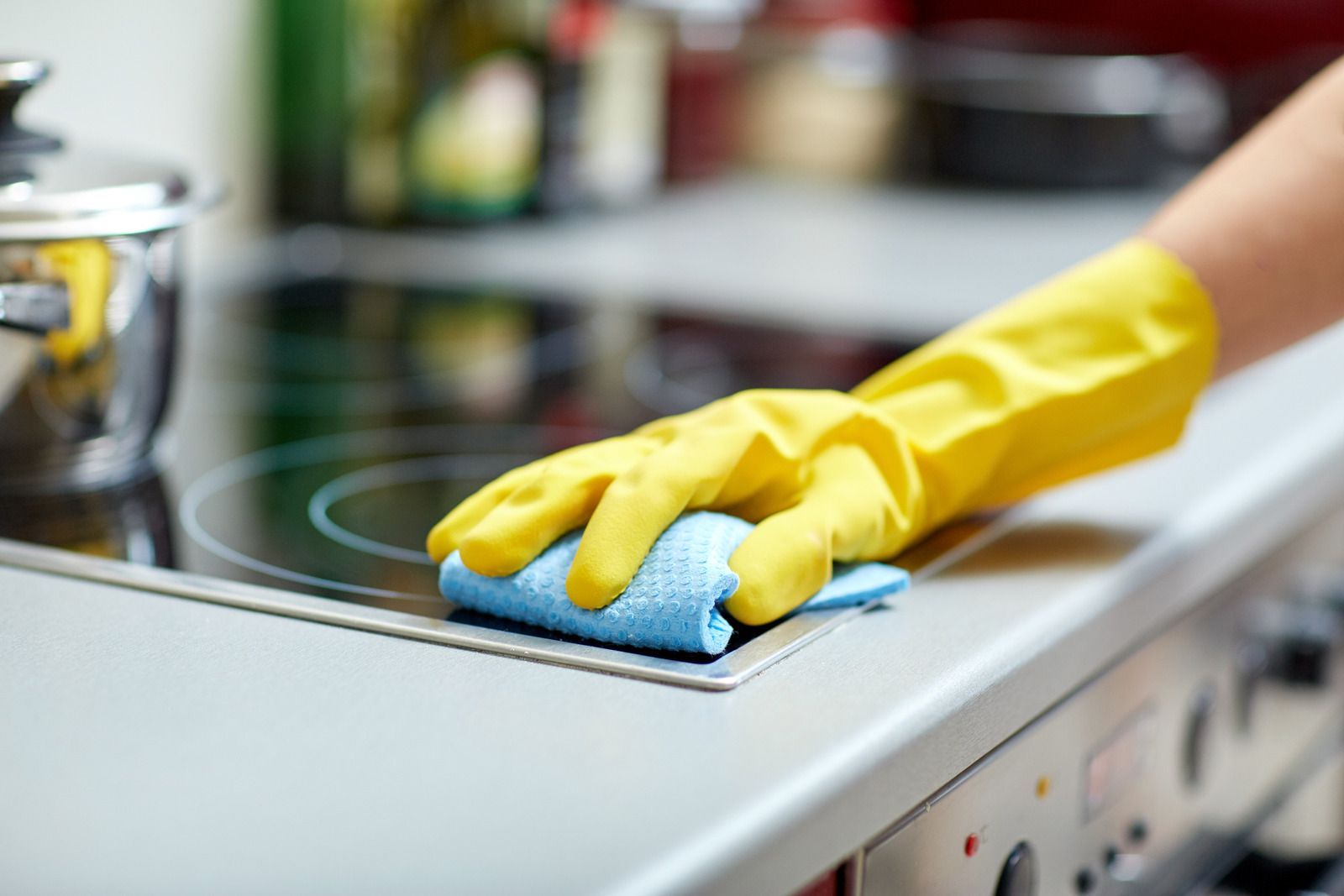 A person wearing yellow gloves is cleaning a stove top with a cloth.