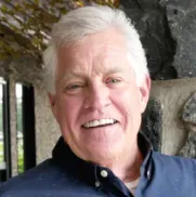 A man with gray hair and a blue shirt is smiling for the camera.