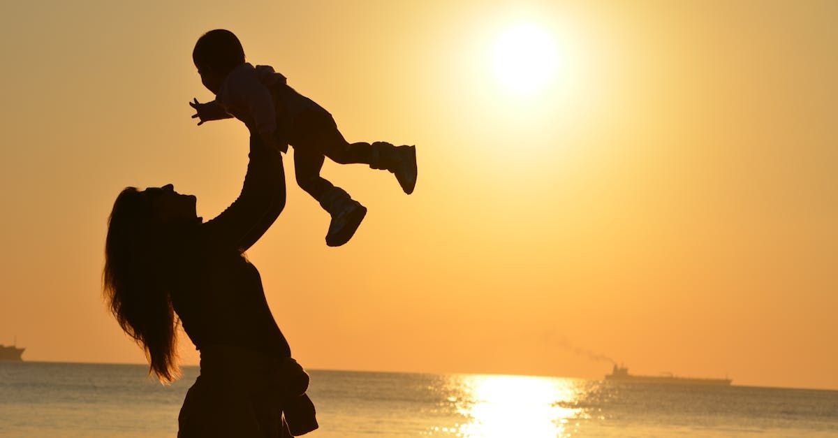 A woman is holding a baby in her arms on the beach at sunset.