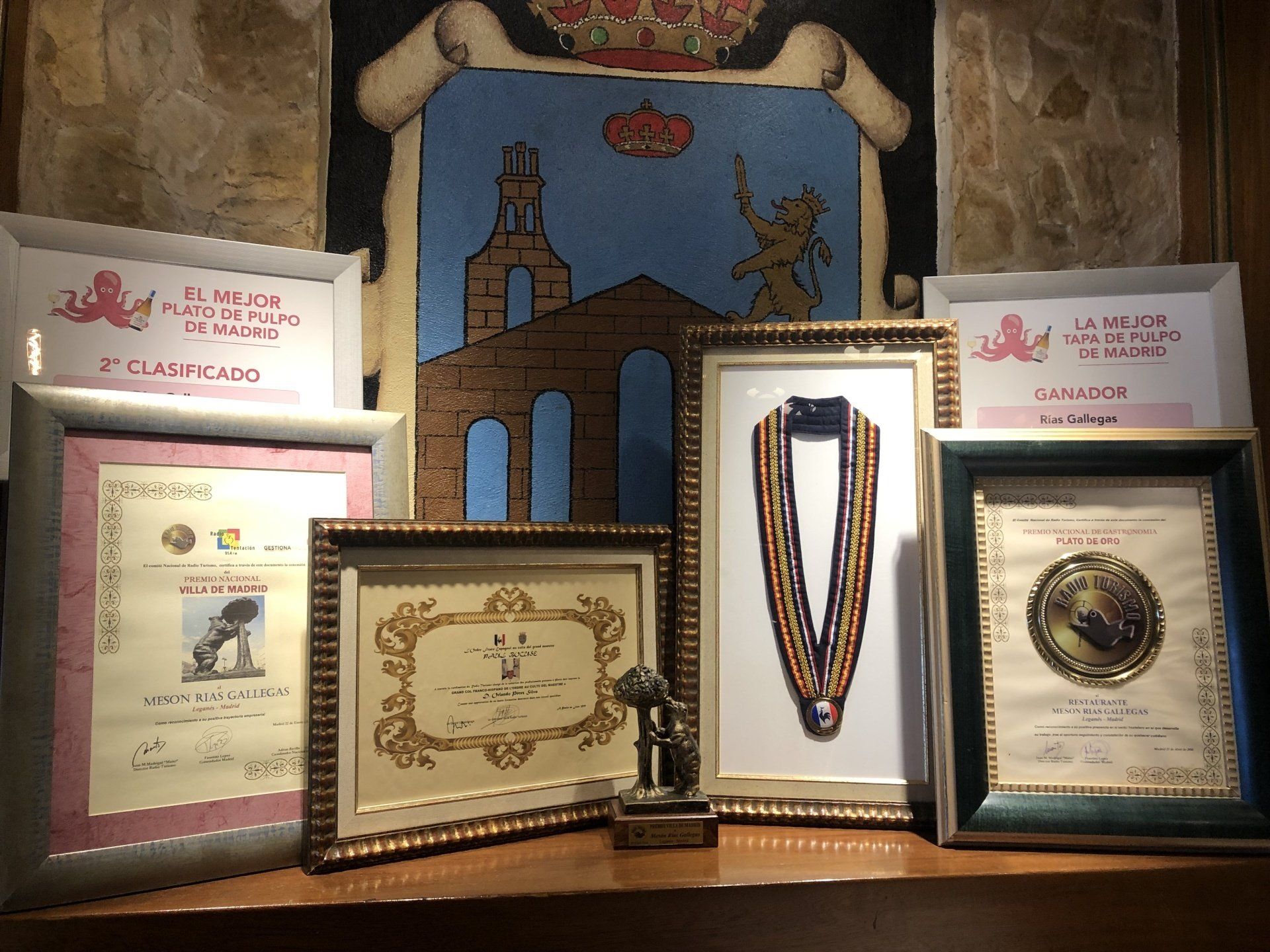 Una exposición de cuadros enmarcados y medallas con un escudo de armas al fondo.