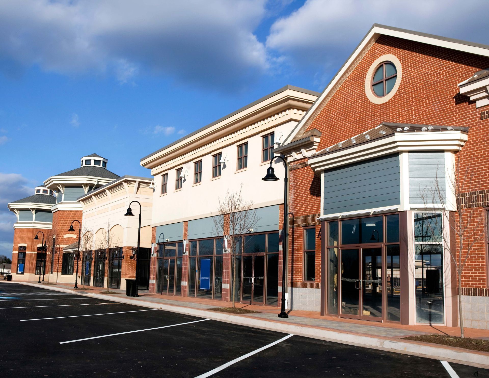Row of empty storefronts in a shopping plaza under a bright blue sky
