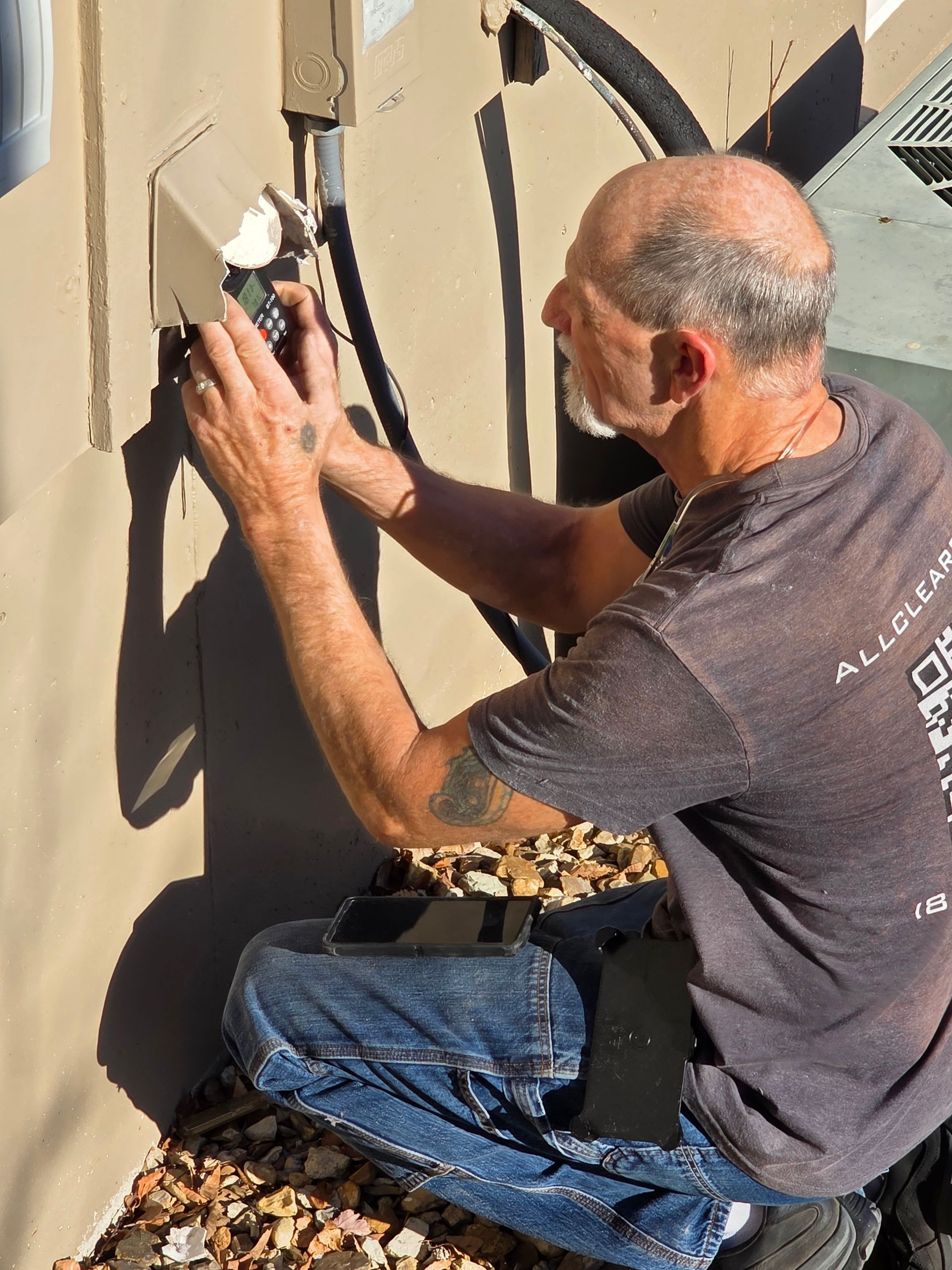 Man painting a tan wall with a roller outdoors, kneeling on a step stool.