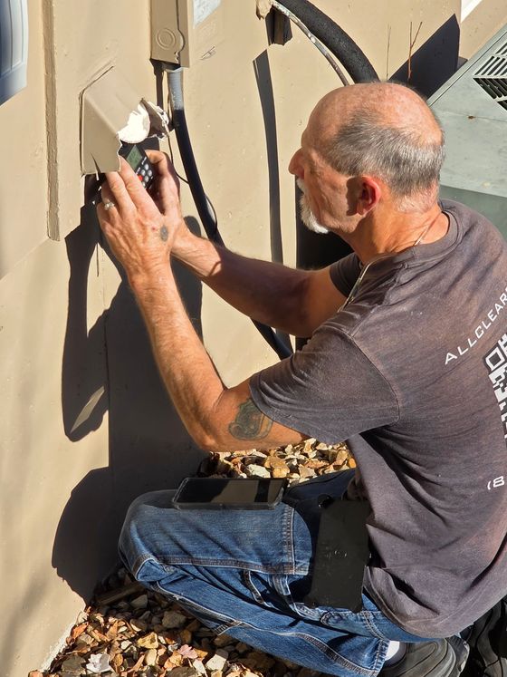 Man kneeling and painting a beige wall with a small roller outdoors in bright sunlight