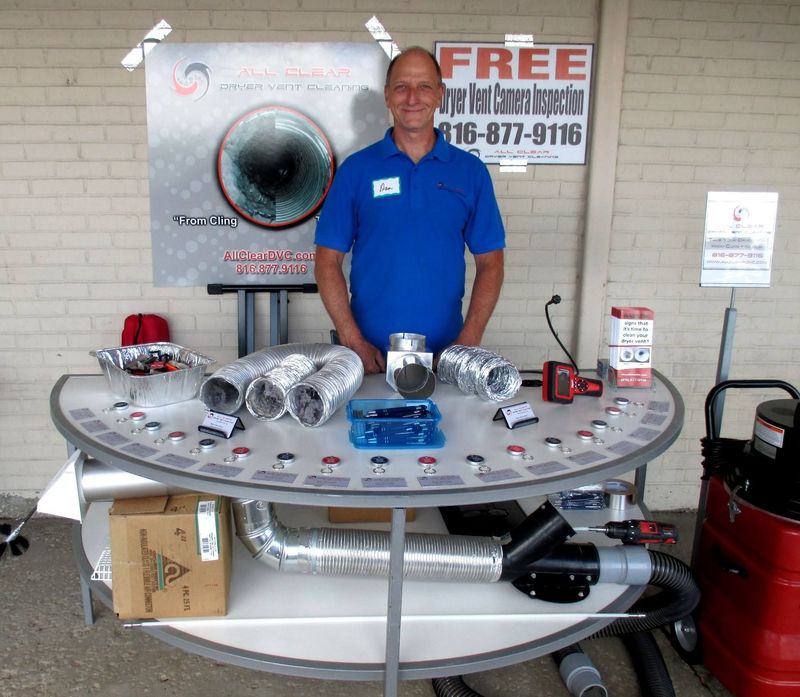 Man in blue polo behind display table with metal ducts and HVAC parts at an indoor trade booth