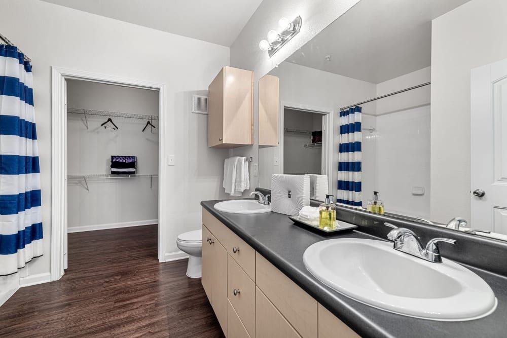 a bathroom with two sinks, a toilet, and a walk-in closet at Marquis at Canyon Ridge in Austin, TX.