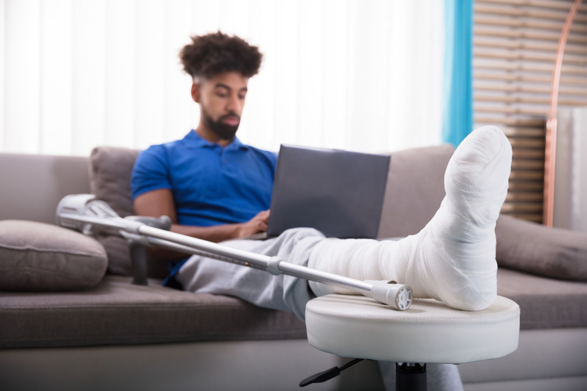 A man with a broken leg is sitting on a couch using a laptop computer.