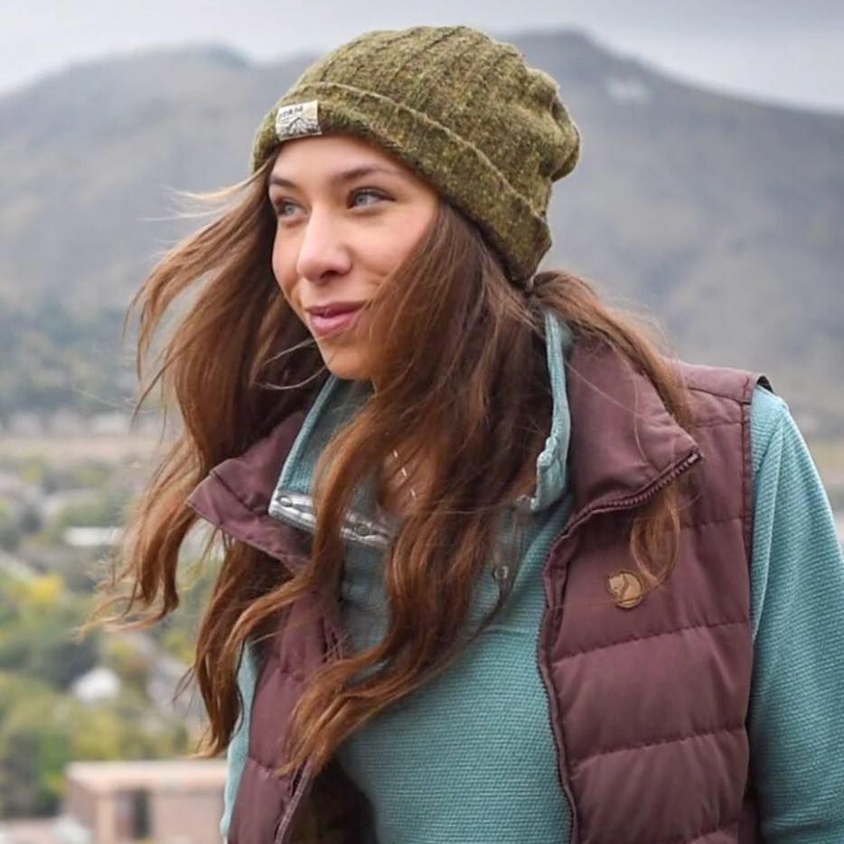 A person wearing a knit beanie and a maroon vest over a blue long-sleeved shirt.
