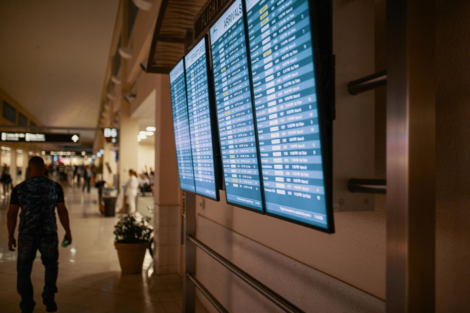 A person walking through an airport terminal past large digital flight information display screens.