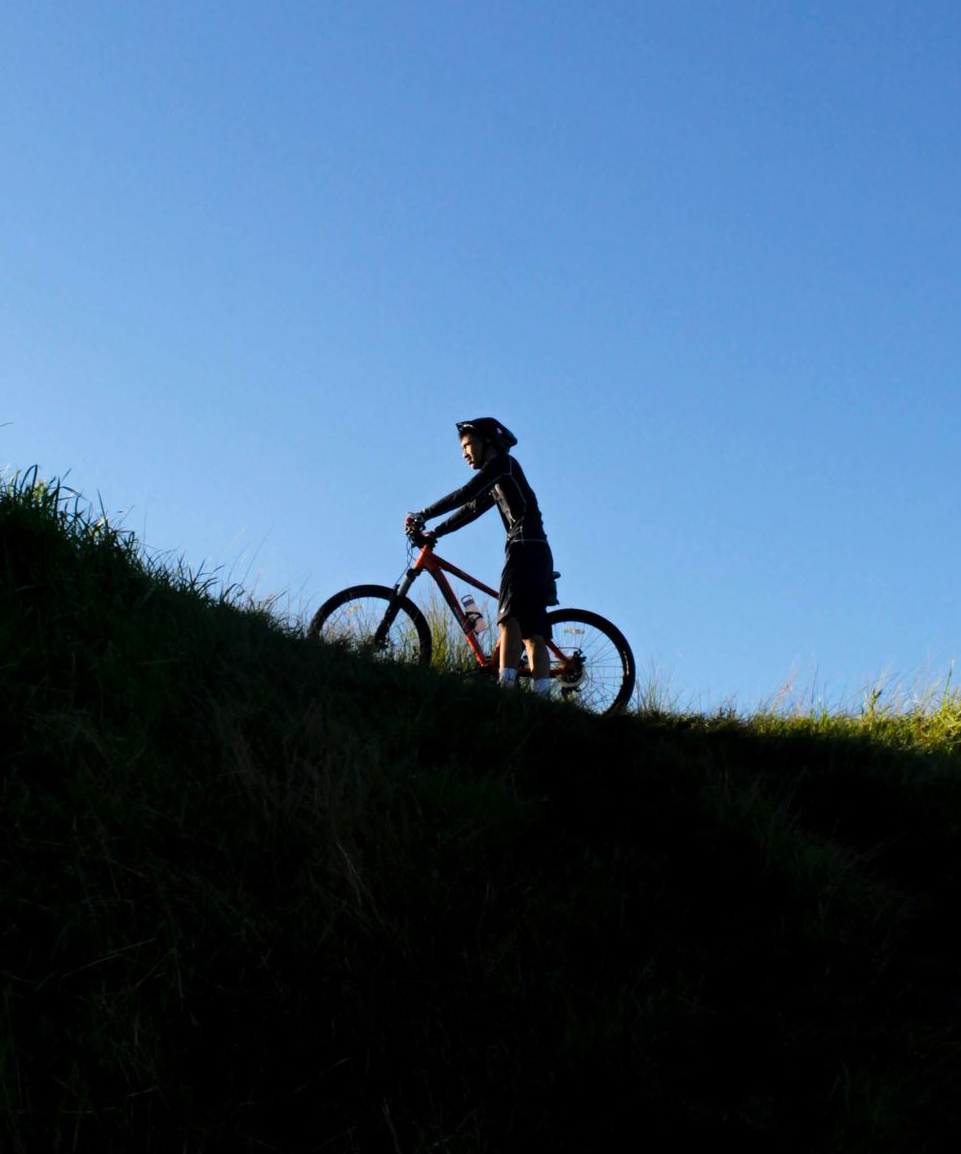 A cyclist rides a mountain bike along a grassy ridge against a clear blue sky.