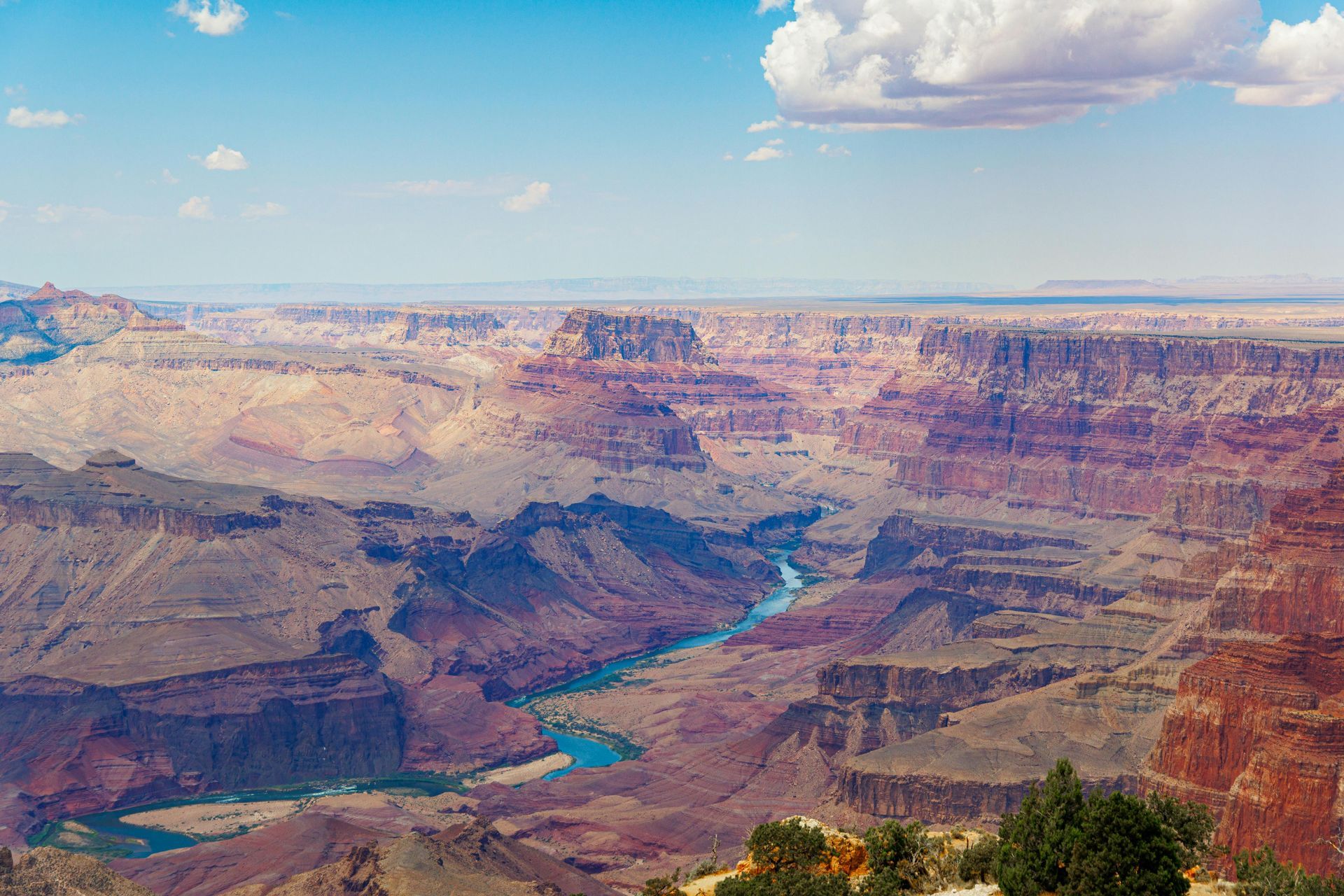A panoramic view of the Grand Canyon, featuring layered red rock formations and the Colorado River winding through.