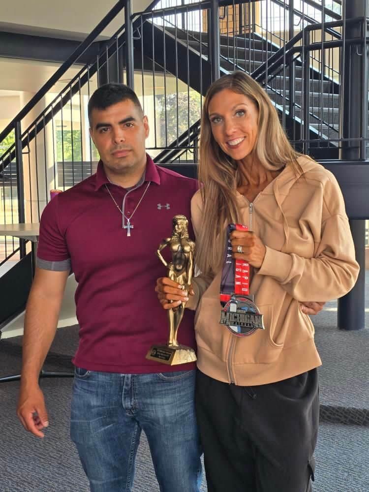 A man and a woman standing next to each other holding trophies.