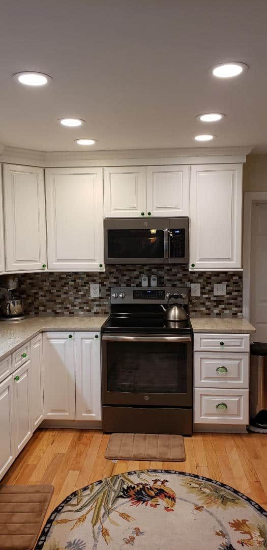 A kitchen with white cabinets , a stove , a microwave , and a rug.