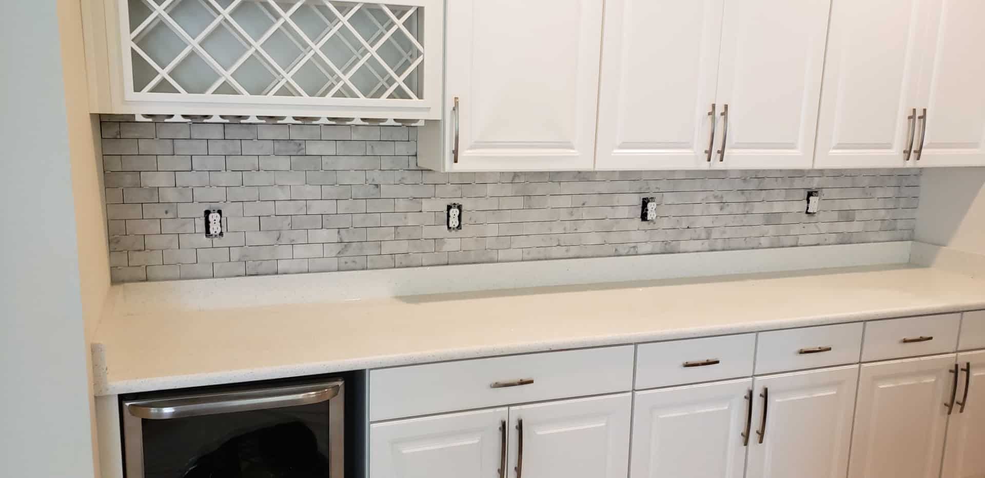 A kitchen with white cabinets , white counter tops , and a wine rack.