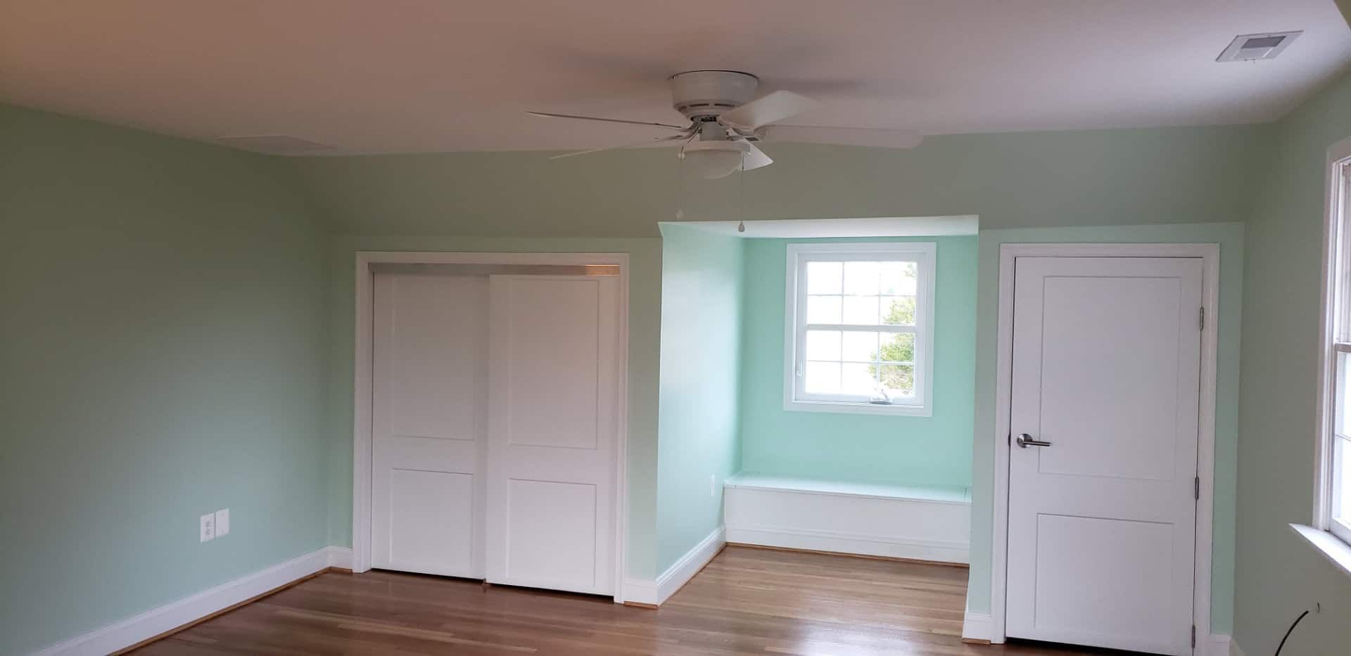 An empty room with green walls and white doors and a ceiling fan.