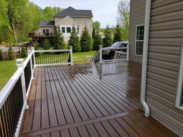 A large deck with a white railing and a house in the background