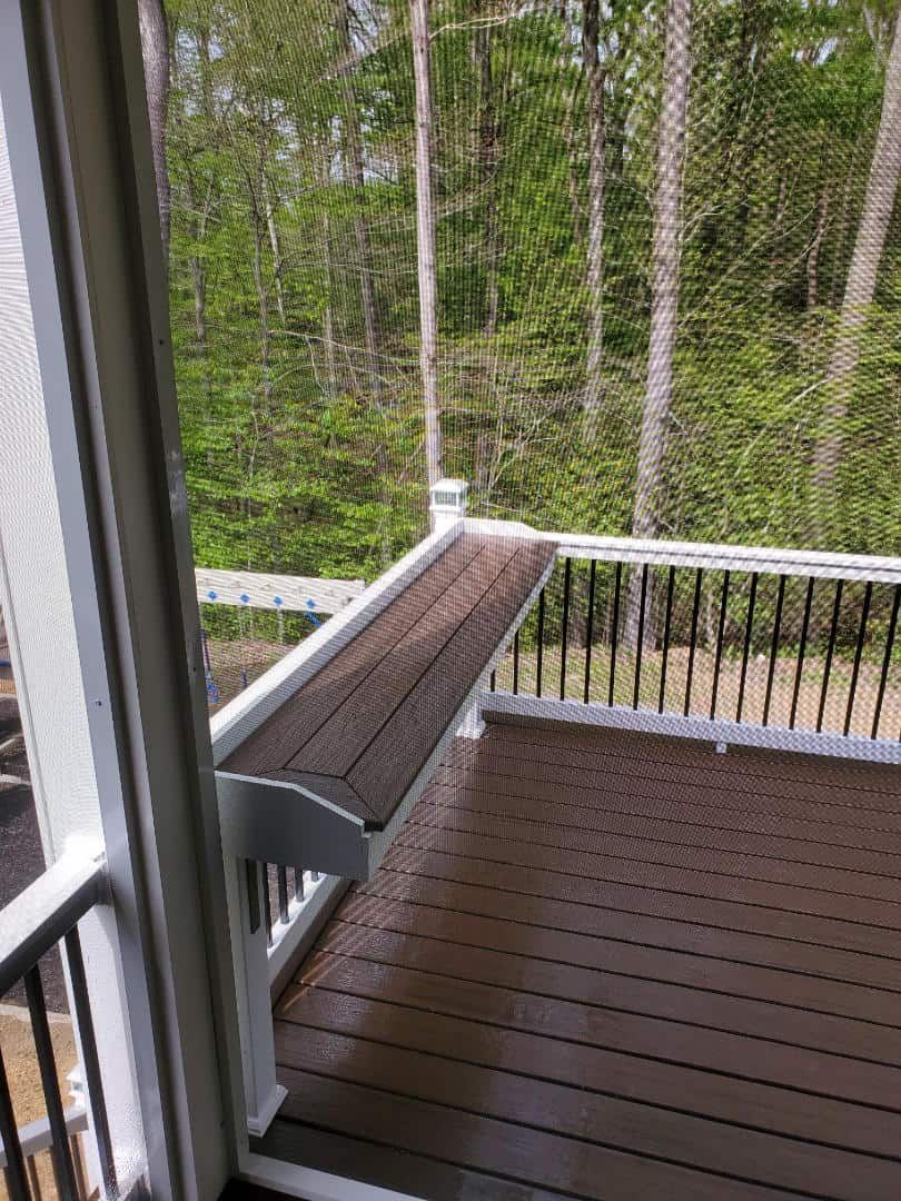 A wooden deck with a bench and trees in the background.