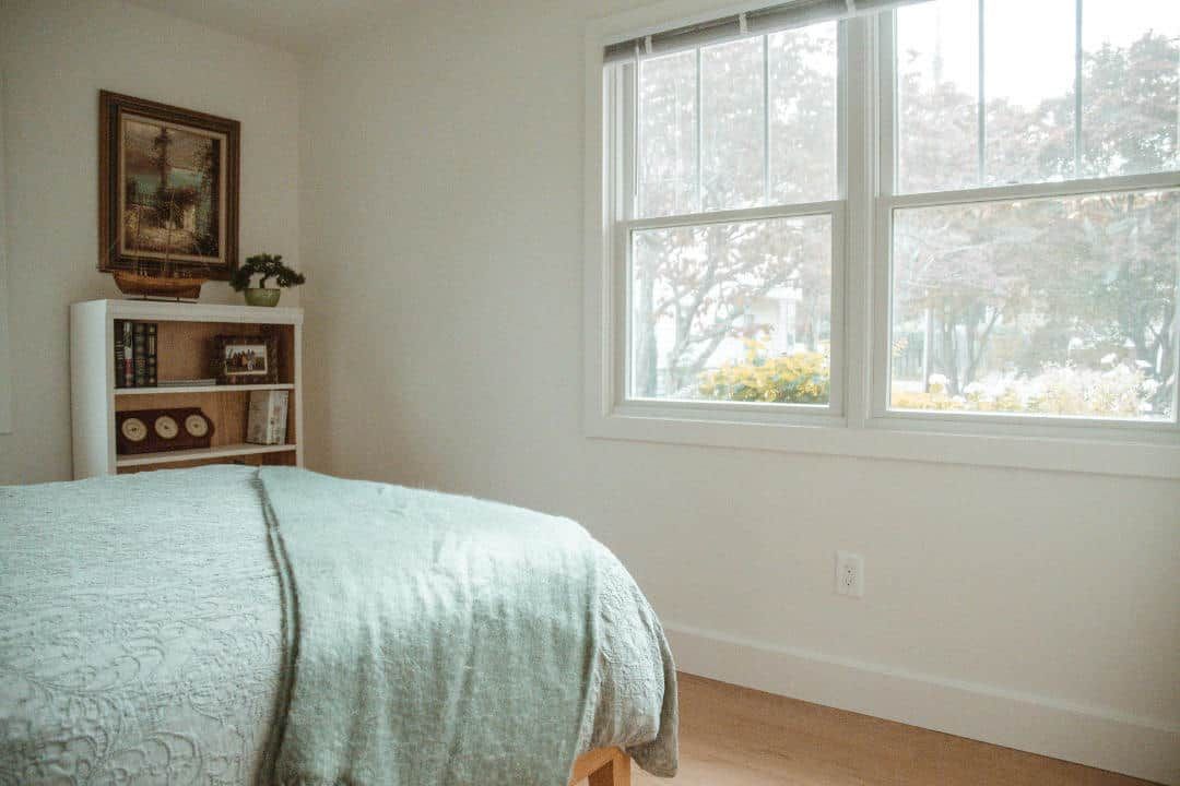 A bedroom with a bed , bookshelf , and two windows.
