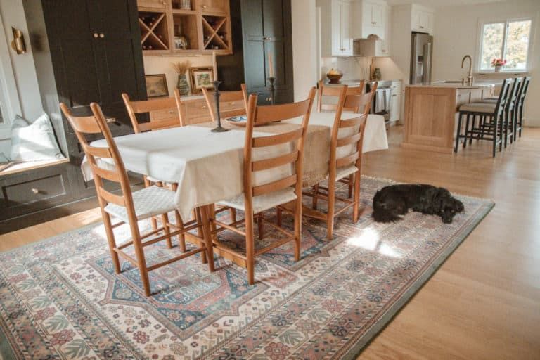 A dining room with a table and chairs and a dog laying on the rug.