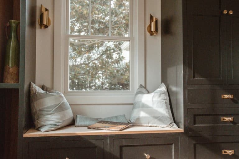There is a window seat with pillows and a book on it.