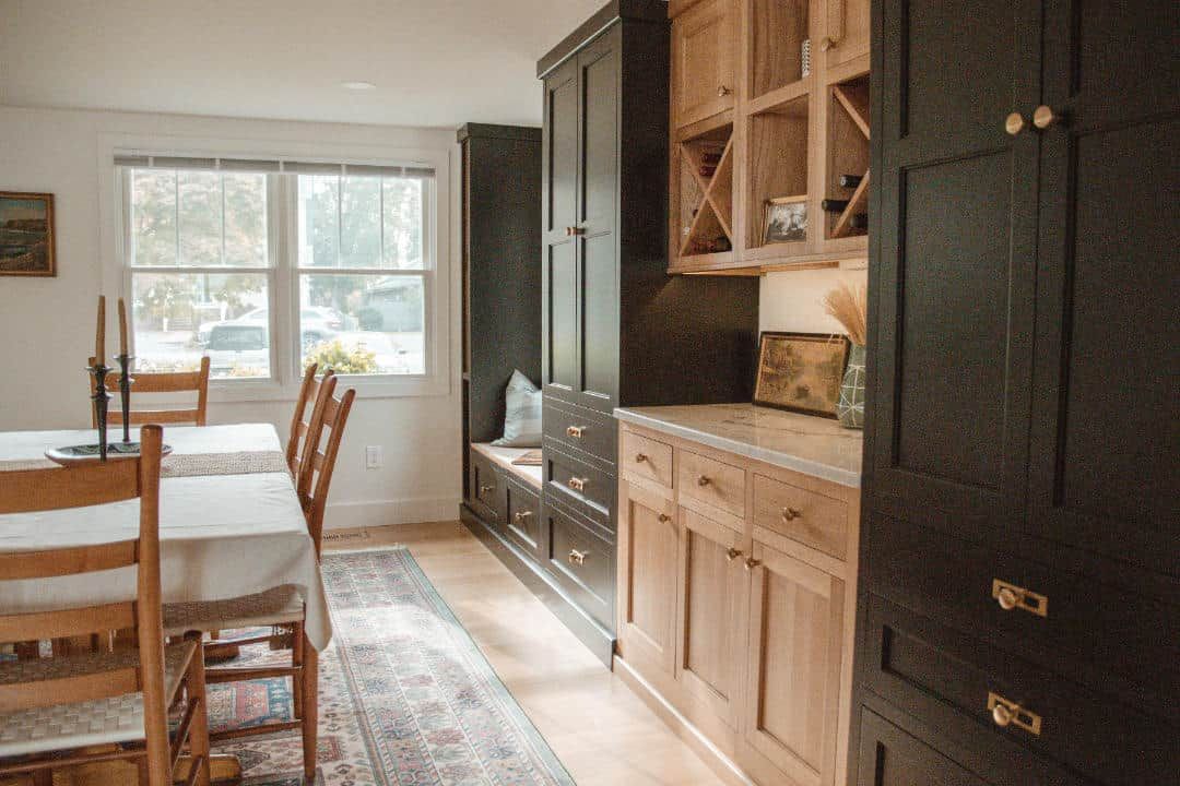A dining room with a table and chairs and a kitchen with black cabinets.