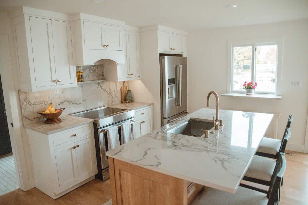 A kitchen with white cabinets , marble counter tops , stainless steel appliances and a large island.