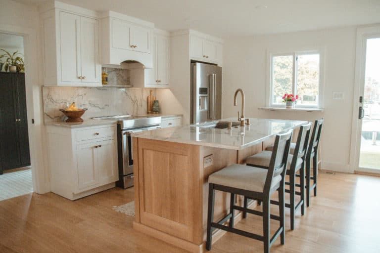 A kitchen with white cabinets , stainless steel appliances , a large island and stools.