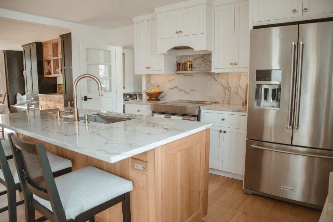 A kitchen with stainless steel appliances , white cabinets , marble counter tops , and a large island.