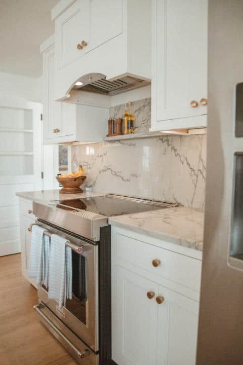 A kitchen with white cabinets , stainless steel appliances , and marble counter tops.