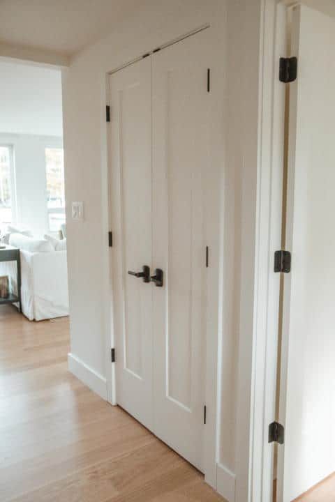 A hallway with a white door and black handles leading to a living room.