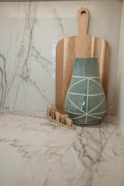 A green vase is sitting on a marble counter next to a wooden cutting board.