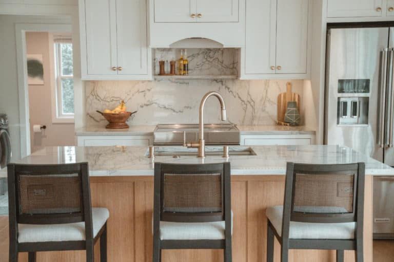 A kitchen with white cabinets , stainless steel appliances , a sink , and three chairs.