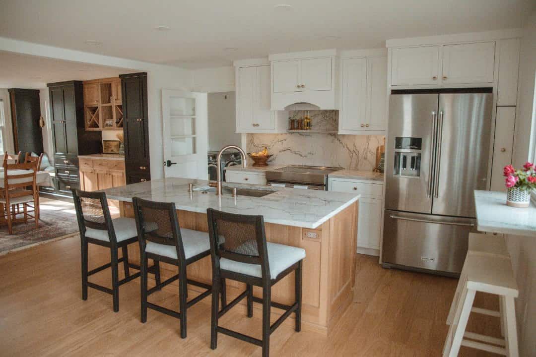 A kitchen with a large island , stools , a refrigerator and a sink.
