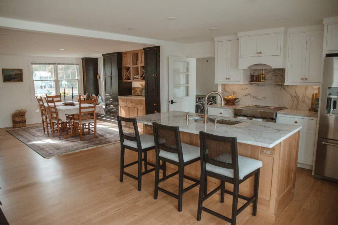 A kitchen with a large island and stools and a dining room in the background.