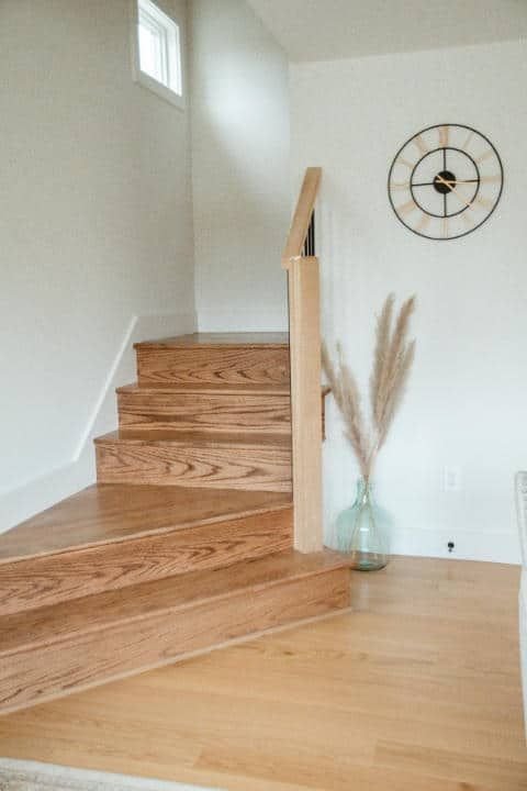 A wooden staircase with a clock on the wall next to it.