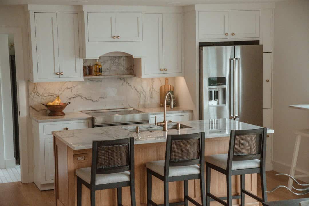 A kitchen with white cabinets , a stainless steel refrigerator , a stove , a sink and a bar.